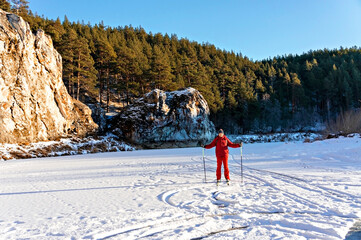 Young man in red winter clothes skiing along the frozen snowy river near beautiful cliffs. Winter...