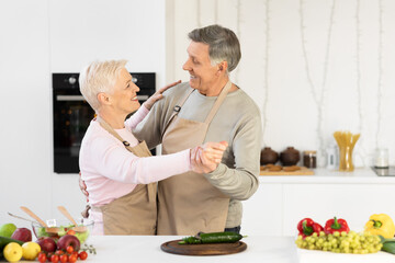 Cheerful Elderly Couple Dancing In Kitchen Having Fun At Home