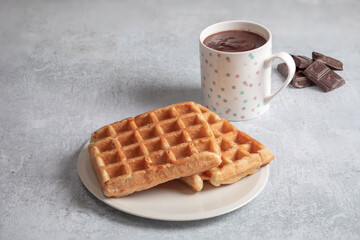 Two homemade waffles with a cup of hot chocolate over a white table.