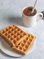 Two homemade waffles with a cup of hot chocolate over a white table.