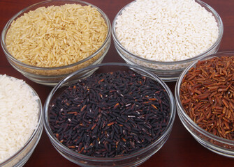 Assortment of rice in glass bowls close up - white, brown, red and black rice.