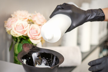 Hairdresser's hand mix hair dye in a black bowl in a beauty salon