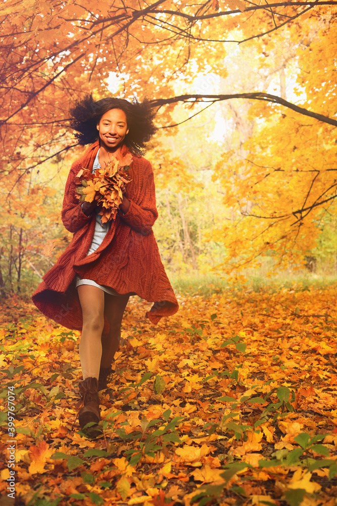 Wall mural Young black woman throwing autumn leaves in the autumn forest