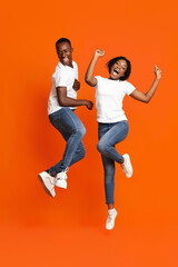 Fototapeta na wymiar Carefree african man and woman dancing on orange
