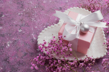 A gift box with a pink ribbon on a white saucer-shaped plate and a gypsophile. The concept of Valentine's Day, anniversary, Mother's Day and birthday greetings, has a copy of the space