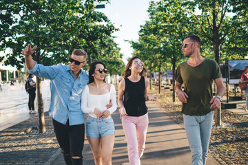 Group of hipster guys 20 years old enjoying weekend meeting for walking together and communicate, trendy dressed male and female in sunglasses talking during sincerely conversations at city street