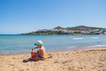 Fototapeta na wymiar Menorca, Spain - August 6, 2020: Baby girl playing in a beach. Cala Tirant, Fornells, Menorca, Balearic Islands. Spain.