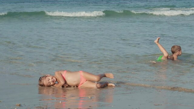 Wide shot of Caucasian boy and his little cute sister wearing swimming suits having fun and swimming in the ocean