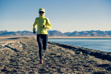 Woman trail runner cross country running on winter high altitude lakeside