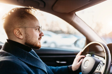 male driver in business attire drives a car in winter on a sunny day. business trip behind the wheel