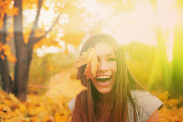 Casual joyful woman having fun throwing leaves in autumn at city park.