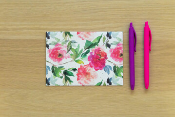 A flat lay photo of a postcard with a flower pattern and two pens