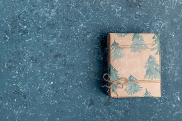 One gift box wrapped in festive Xmas wrapping paper on turquoise textured background. Safe delivery of Xmas presents. Christmas DIY presents. Christmas or New Year backdrop. Top view. Copy space.