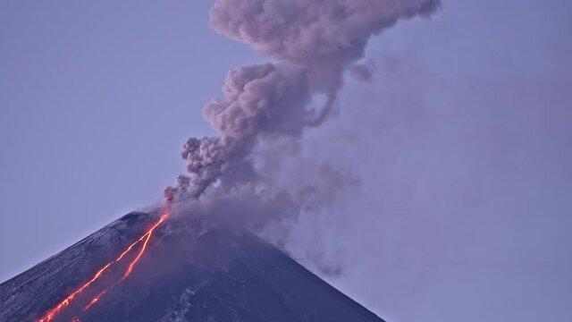 Eruption of Klyuchevskaya Sopka or Klyuchevskoy volcano on Kamchatka. Big pillar of volcanic smoke and burning lava erupting from vent. Early winter morning. Concept of wild nature and geology.