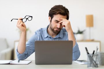 Tired Man At Laptop Massaging Nosebridge Holding Eyeglasses In Office