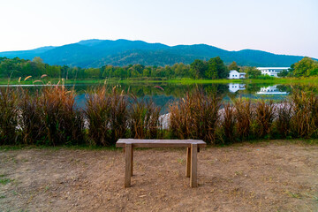 wood bench with beautiful lake at Chiang Mai with forested mountain and twilight sky