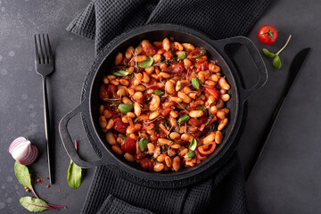 white beans stewed in tomato sauce with onions and herbs in a black pan