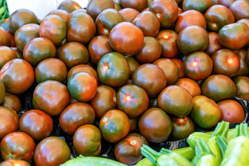 A group of camona tomatoes for sale at an outdoor market, with green courgettes on the corner.