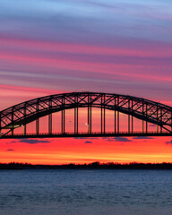 Fototapeta na wymiar Vibrant sunset colors over a steel tied arch bridge. Fire Island Inlet Bridge, Captree State Park New York