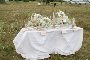 Table with white tablecloth, candlestick and wildflowers in the field