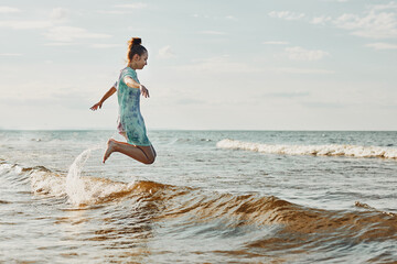 Girl enjoying sea jumping over waves spending a free time over sea on a beach at sunset during summer vacation