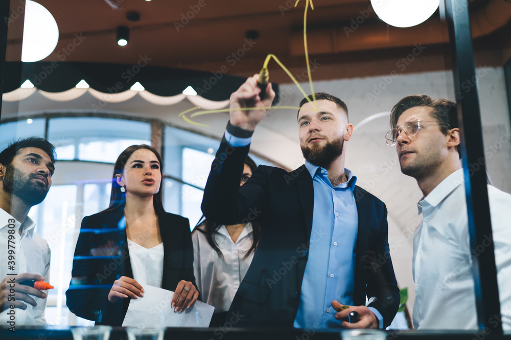 Wall mural Serious multiethnic colleagues drawing on glass window