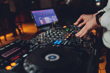 DJ's hand over the laptop and mixing console controlling the sound settings.