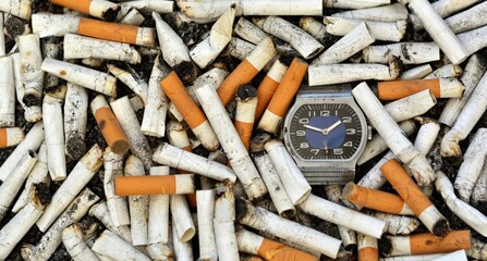 Clock on the background of a pile of cigarette butts with ashes. The concept of shortening life and wasting time on smoking