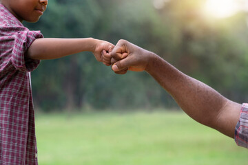 African child  boy bumping fists with his father at park, man and child giving fist bumping
