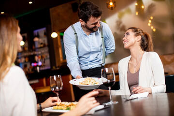Young waiter serving food to female customers in the restaurant