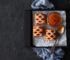 Puff pastry with apricot jam sprinkled with sugar and jam jar with a spoon on white paper on a black background with space for text. Top view © Rika777