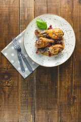 Baked chicken drumstick with apple jam in a light dish on rustic wooden table surface, top view, copy space.