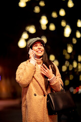 Pretty young woman using her mobile phone in the street at Christmas time