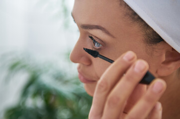 Closeup of a brunette woman applying mascara at her lashes. Makeup concept