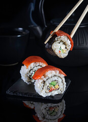 Sushi mit Lachs auf einem schwarzen Hintergrund mit Stäbchen im Hintergrund.