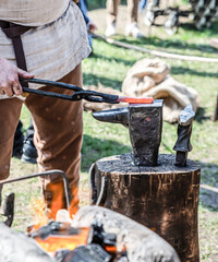 blacksmith in medieval clothes forges hot metal in tongs on the anvil