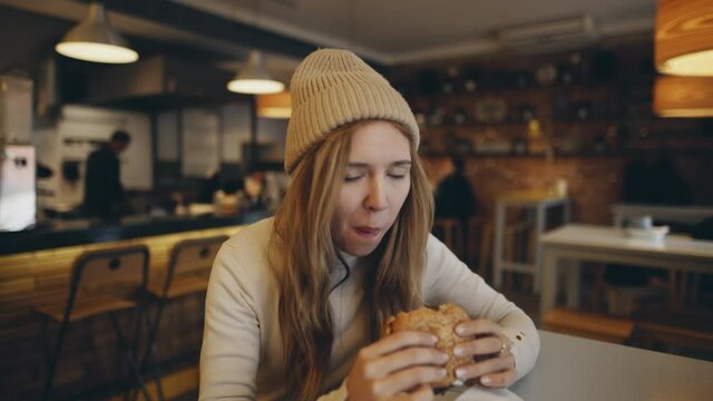Young woman eating burger in fast food restaurant. American style. People eat unhealthy meal. Getting satisfaction from unhealthy food. Junk food, modern life concet.