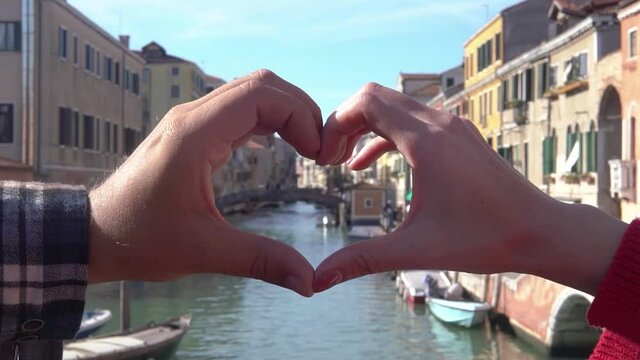 Male and female hands showing heart shape on the background of beautiful view of Venice. Symbol of love. Couple relationship, travel, family concept. Romantic picture of freedom.