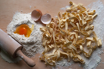 
Homemade pasta lying on the board along with semi-finished products such as flour, a broken egg.