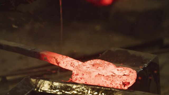 Master Swordsmith working a glowing hot ingot then back on forge to reheat.