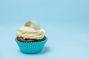 Cupcake with rainbow decoration. Buttercream frosting like cloud. Light blue background
