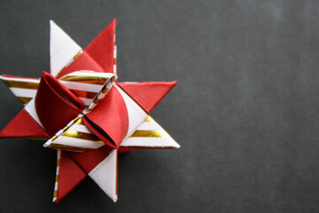 Red, white and gold colored paper christmas star on a dark background.