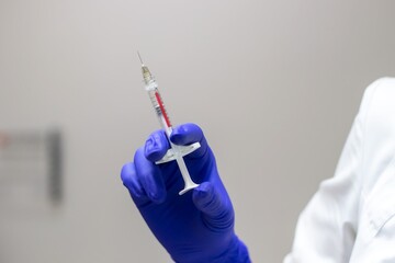 Close-up of the doctor's hands, wearing blue sterile gloves, holding a syringe ready for vaccination.