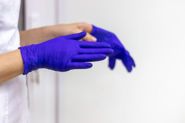 A doctor in a white lab coat puts on a pair of sterile blue gloves. Hands close-up.