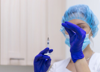 Obraz premium A doctor in a white medical uniform and sterile blue gloves opens a medical syringe with a needle. Hands close-up. Selective focus.