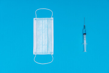 2021 logo made from a medical mask and a syringe with a vaccine. As a symbol of the pandemic and the release of the drug in 2021. Blue background