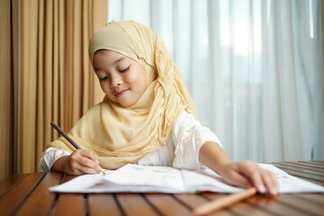 Muslim student child girl writing on the paper book. Asian genius student doing a homework at home. education , study and learning concept. 