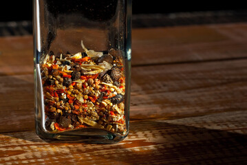 A mixture of various spices in a glass jar close up. Spices on a black, old shabby board. Free space and copy space for text near condiments. Contrasting dramatic light as an artistic effect.