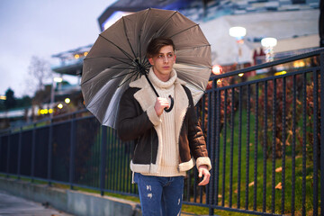 Man taking a walk in hand in the evening rainy weather. Young male taking an umbrella for a walk in the cold and rainy winter weather