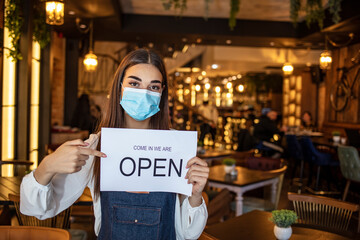 Small business owner with face mask holding the sign for the reopening of the place after the quarantine due to covid-19. Woman with protective mask holding sign we are open, support local business.